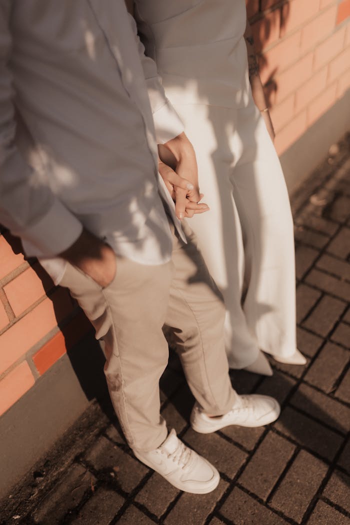 A couple holding hands facing a brick wall, casting soft shadows.